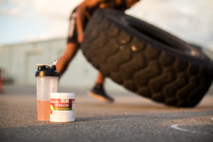 A motivated woman flips a tire. Red Leaf Pre-Workout Energizer is pictured in front